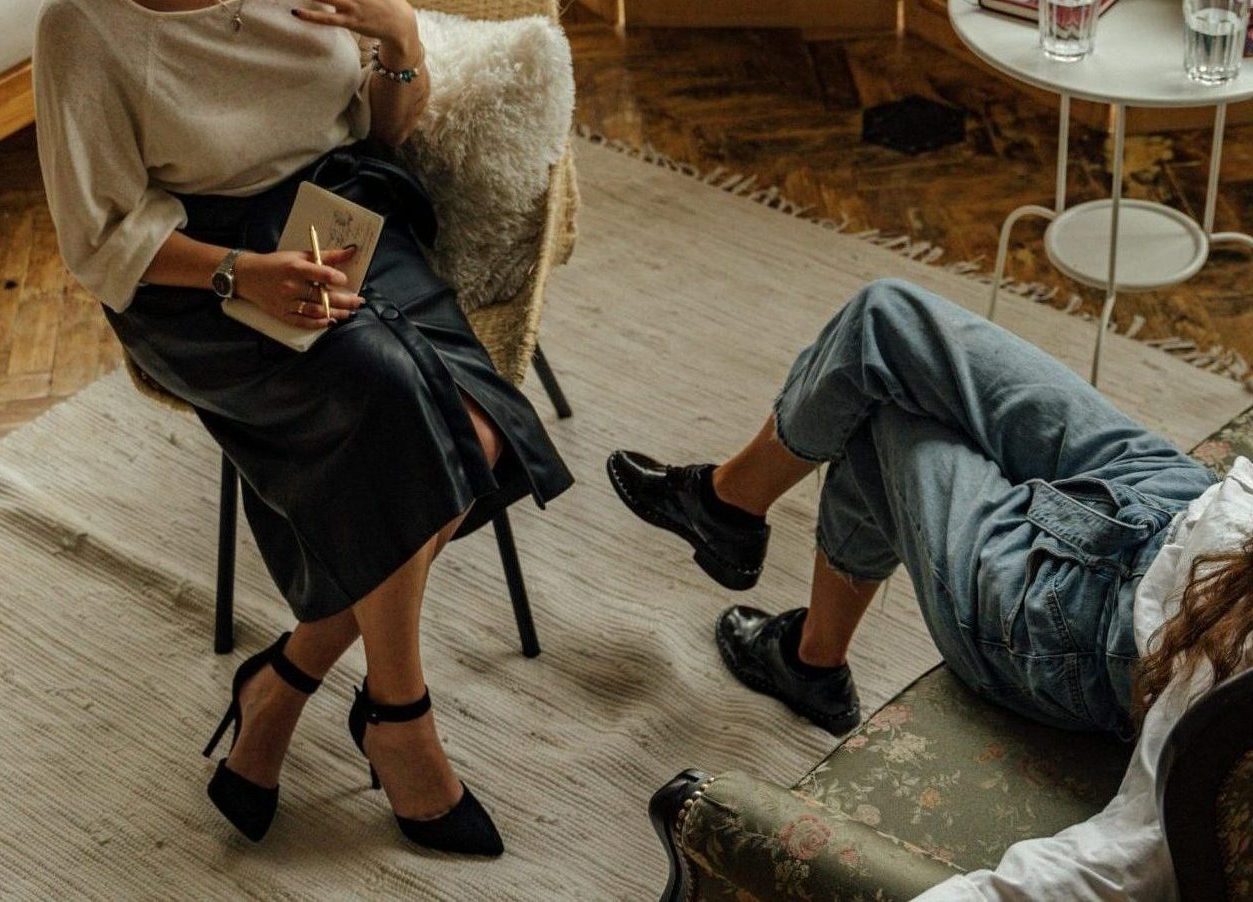 Two women engaged in a psychotherapy session in a warm, inviting interior with plants and natural lighting.