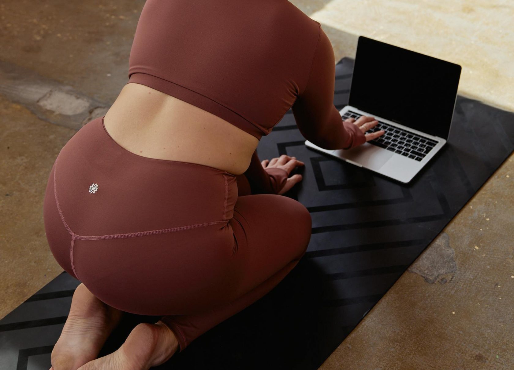 Woman practicing yoga at home using a laptop for guidance on her yoga mat.